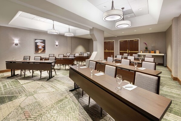 Un salón de conferencias con largas mesas, sillas y luminarias modernas.