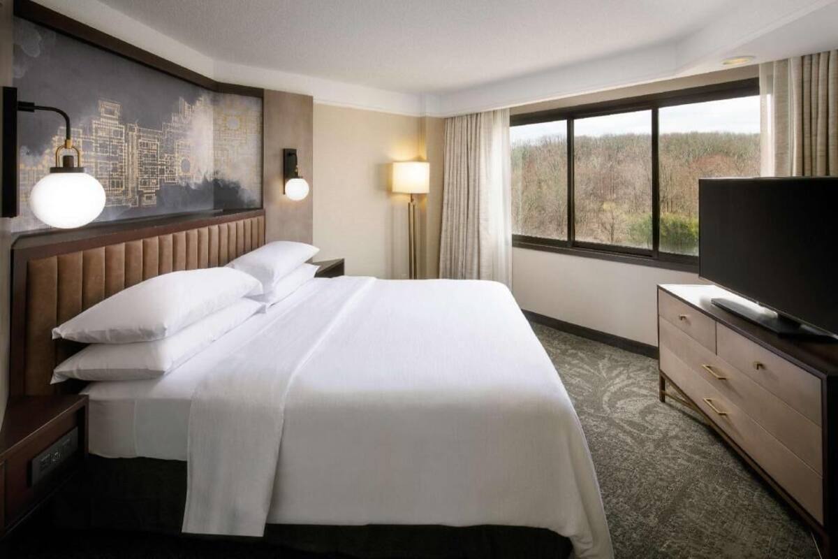 Habitación de hotel con cama, televisión, escritorio y un ventanal con vistas.