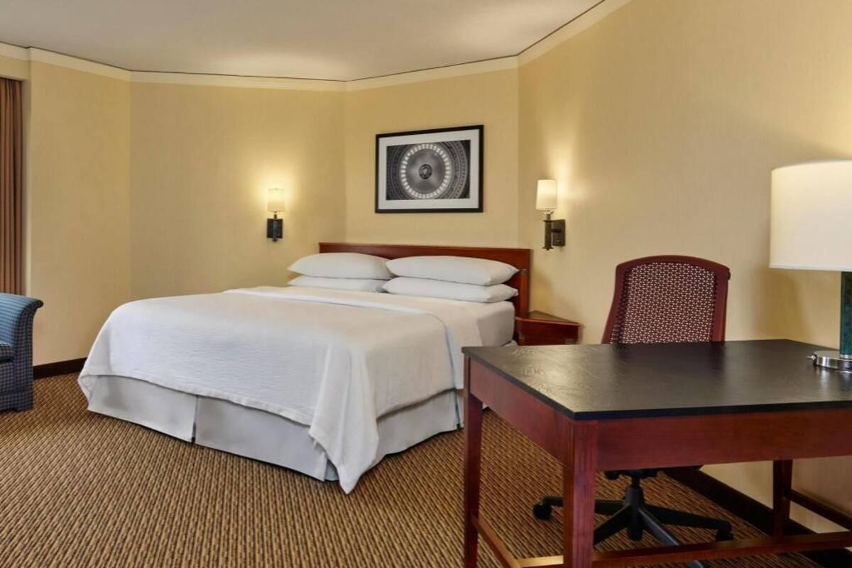 A hotel room with a bed, a desk, a chair, and a wall-mounted picture.
