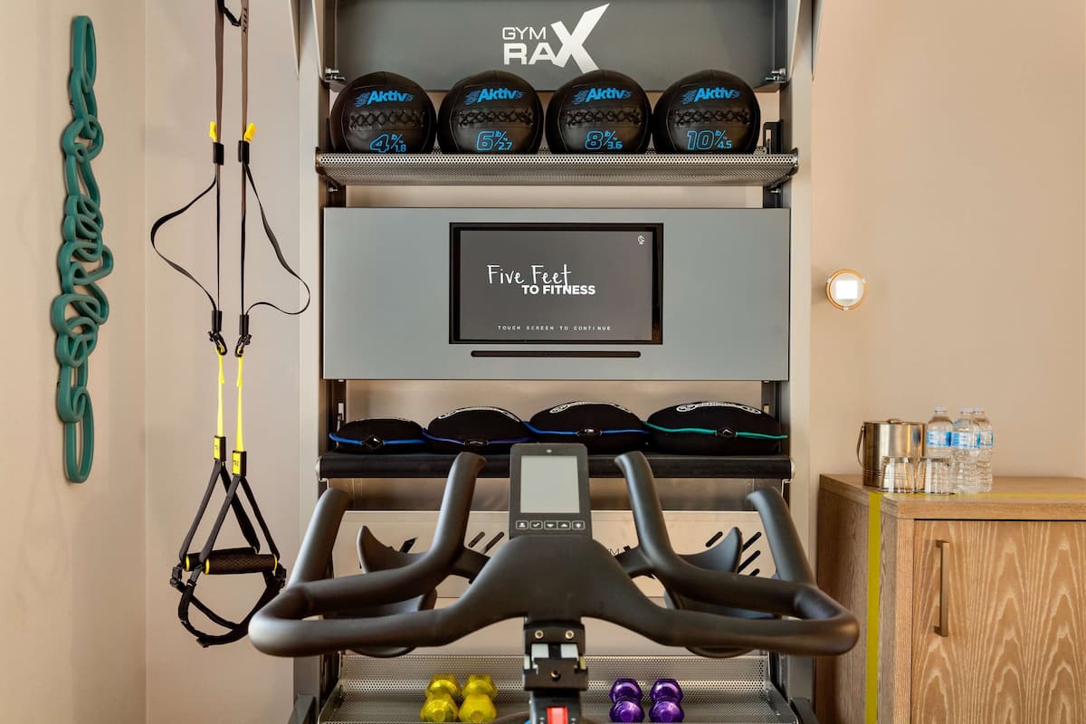 Un gimnasio con una bicicleta estática, bandas de resistencia y una pantalla que muestra el texto 'Five Feet to Fitness'.