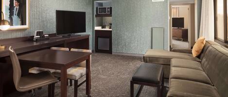 A hotel room with a desk, television, kitchenette, sofa, and a mirror.