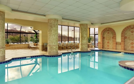 An indoor swimming pool with clear blue water, surrounded by lounge chairs and potted plants.