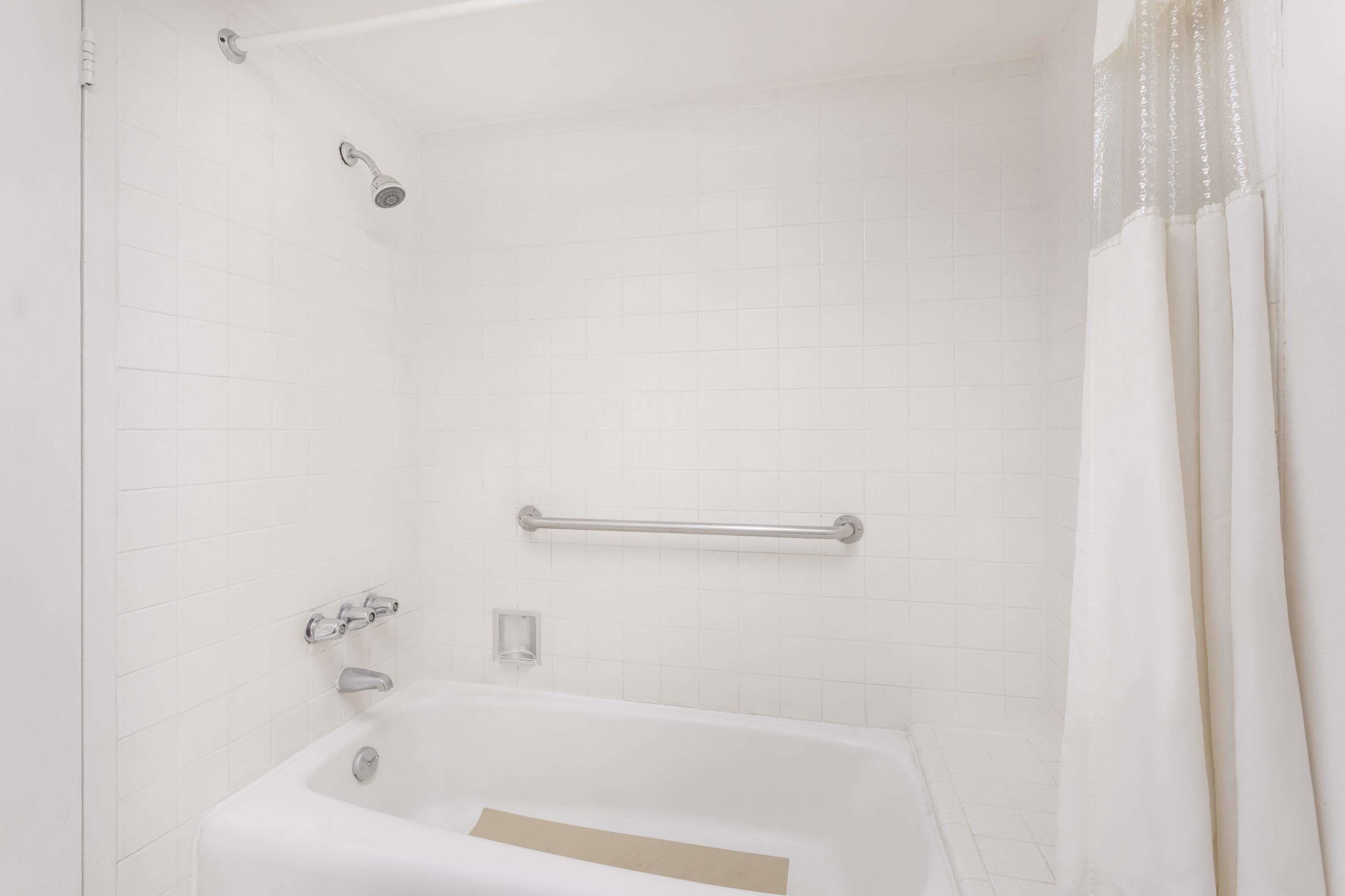 Un baño blanco con bañera, ducha y barra de apoyo.