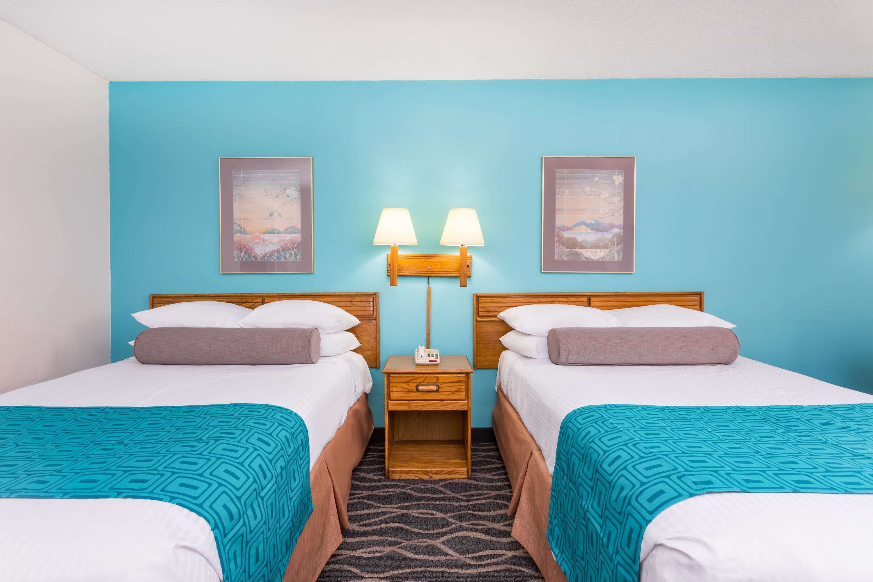 A hotel room with two beds, a nightstand with a lamp, and two framed pictures on the wall.