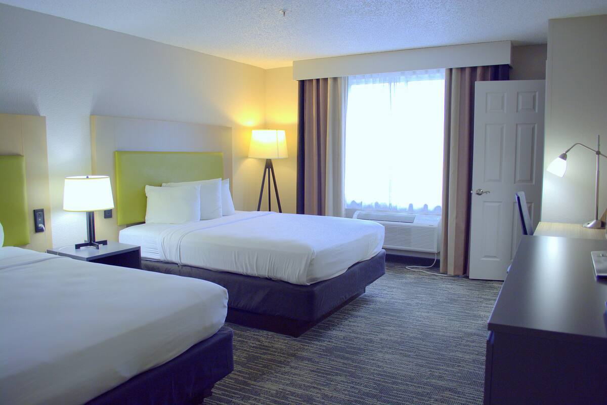 A hotel room with two beds, a desk, a lamp, and a window with curtains.