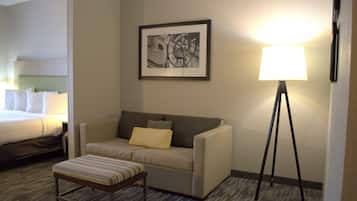 A hotel room with a bed, a sofa, a small table, a floor lamp, and a framed picture on the wall.