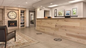 A reception area with a wooden reception desk, a fireplace, and framed artwork on the wall. - Country Inn & Suites by Radisson, Port Clinton, OH (Port Clinton)