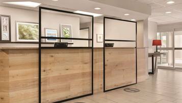 A reception area with a wooden reception desk, framed artwork on the wall, and a red lamp on a side table.