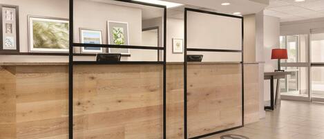 A reception area with a wooden reception desk, framed artwork on the wall, and a red lamp on a side table.
