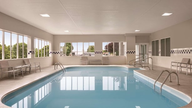 A large indoor swimming pool with clear glass walls, multiple lounge chairs, and a view of the outside. - Country Inn & Suites by Radisson, Port Clinton, OH (Port Clinton)