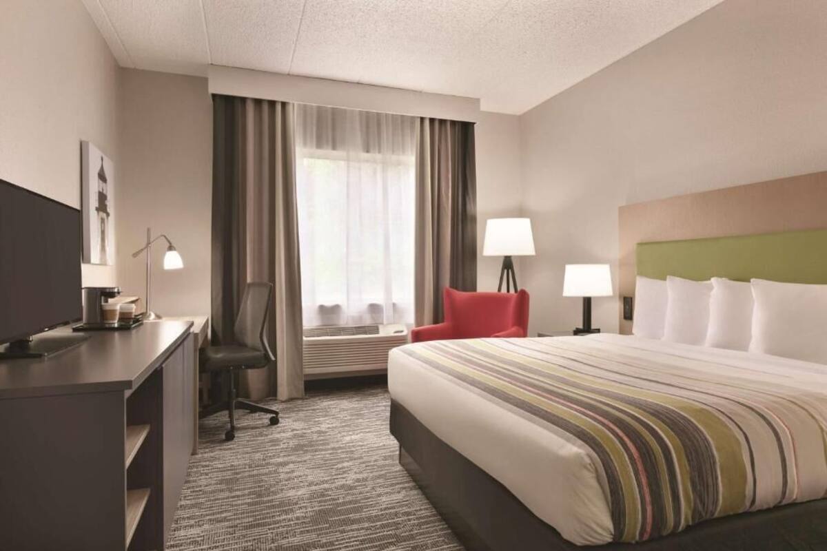 A hotel room with a bed, desk, chair, lamps, and a window with curtains.