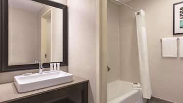 A bathroom with a white sink, a large mirror, a shower with a white curtain, and a framed picture on the wall.