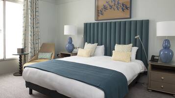 A hotel room with a large bed, two bedside tables with lamps, a chair, a painting on the wall, and a view of the outdoors.