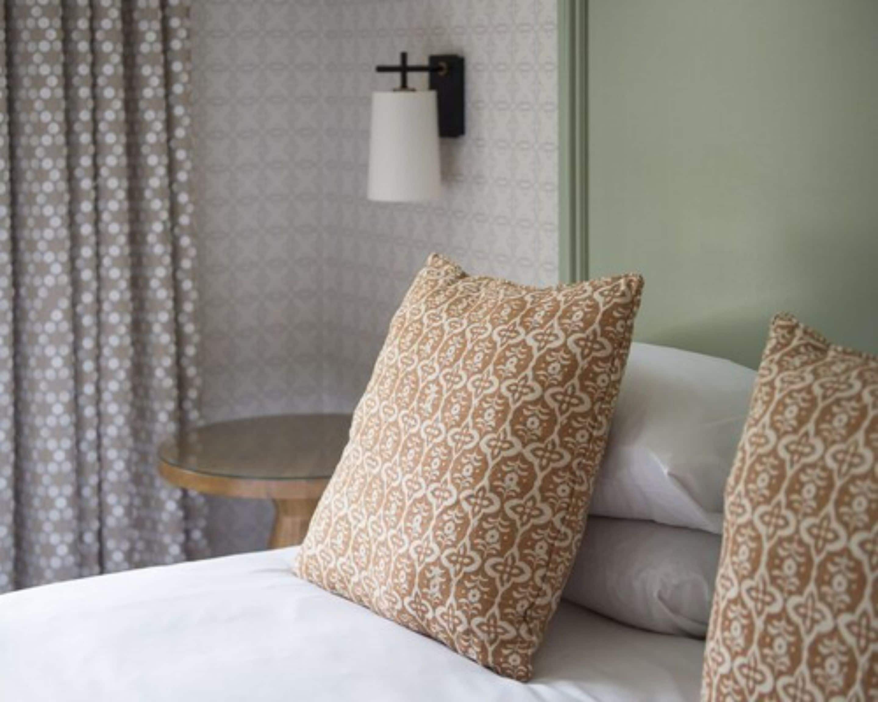 A bed with patterned pillows, a round side table, and a wall-mounted light fixture.