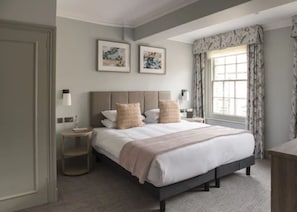 A neatly arranged bedroom with a large bed, bedside tables, and framed artwork on the wall.