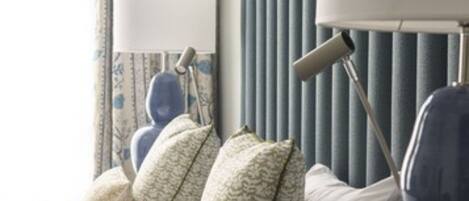 A neatly arranged hotel room with a bed, pillows, a lamp, and a radiator.