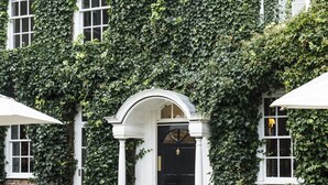 A building with ivy-covered walls, a central entrance with an arch, and outdoor seating with wicker furniture.