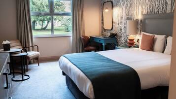 Habitación de hotel con una cama grande, un escritorio, una silla y una ventana con vistas a árboles.