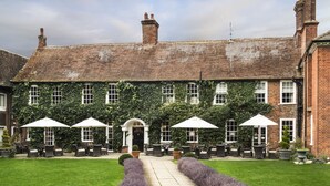 A traditional brick building with ivy-covered walls, outdoor seating with umbrellas, and a well-maintained lawn.