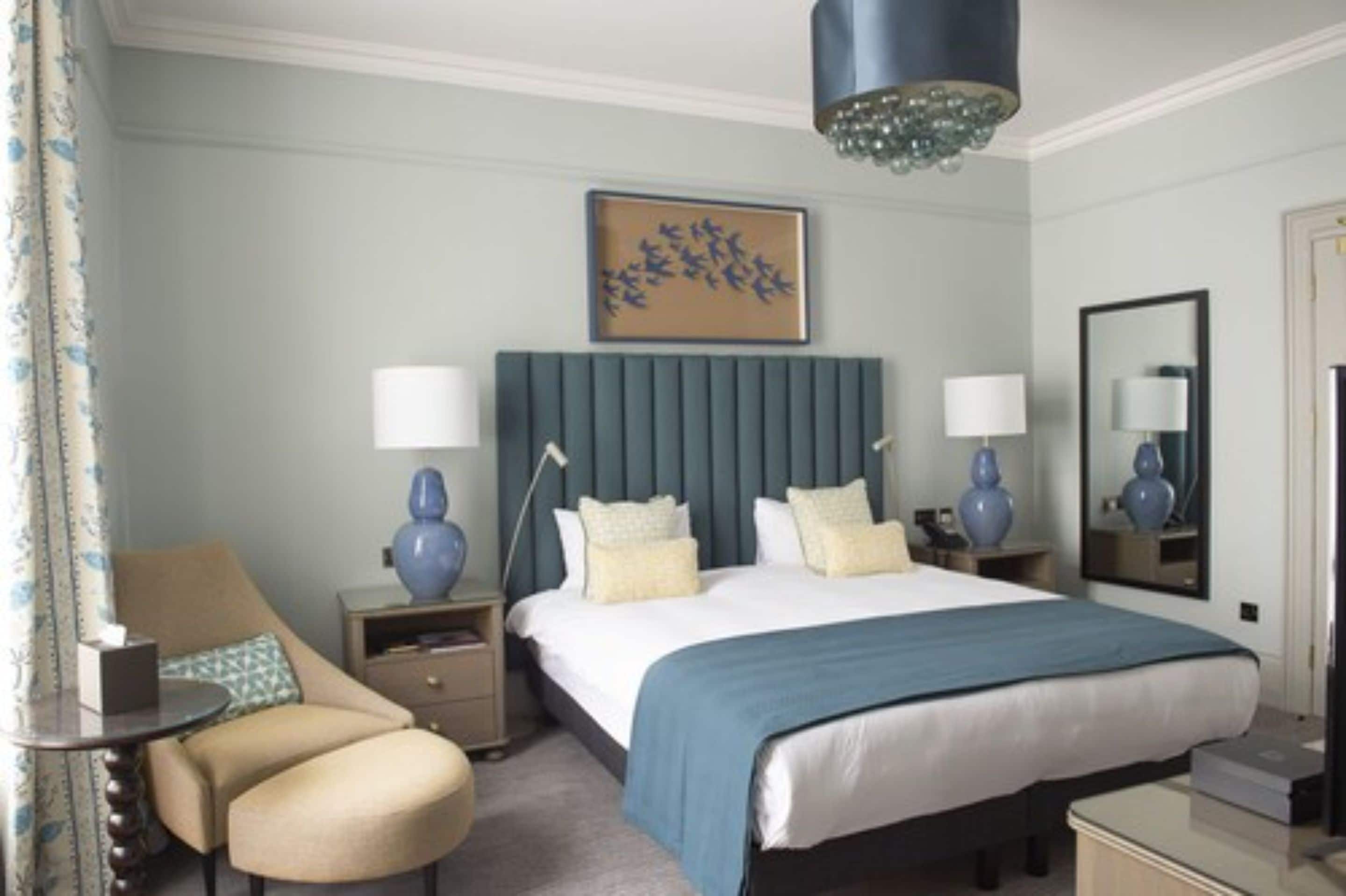 A hotel room with a large bed, two bedside tables with lamps, a chair, a dresser, and a mirror.