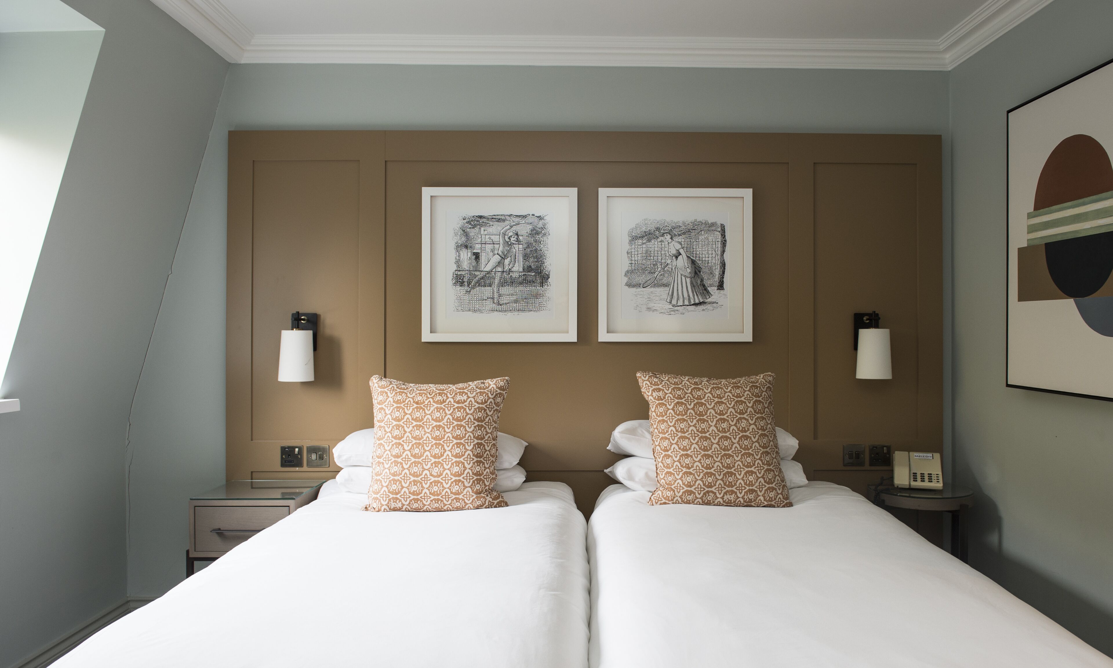 A hotel room with a large bed, two pillows, a nightstand, a lamp, and two framed pictures on the wall.