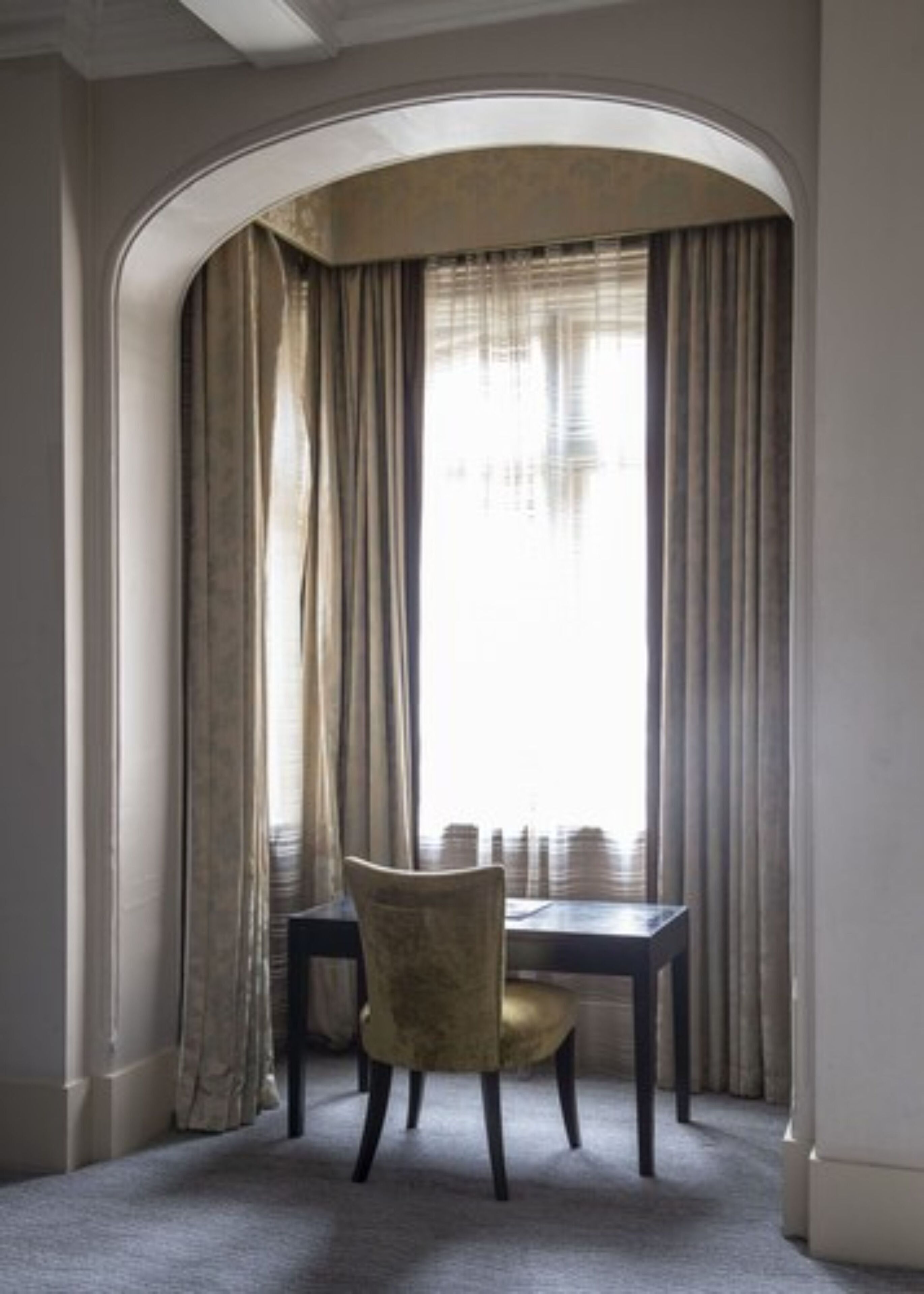 A room with a table and a chair, a window with curtains, and an arched doorway.