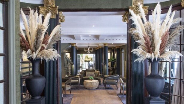 A grand hallway with tall columns, a chandelier, and a seating area with sofas and a coffee table.