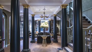 A grand hallway with black columns, a chandelier, and a staircase.