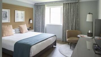 Een hotelkamer met een bed, een bureau, een stoel, een lamp en een raam met gordijnen.