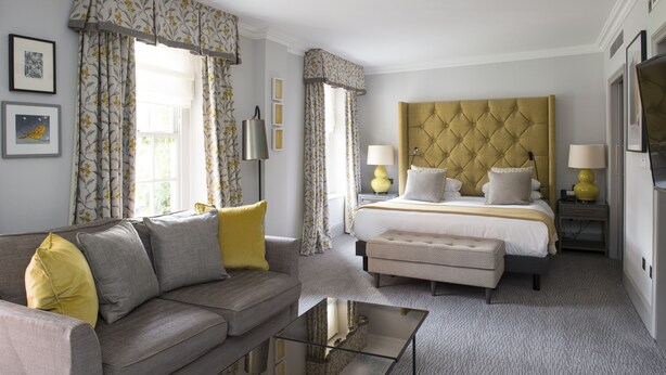 A hotel room with a bed, a sofa, a glass coffee table, and a nightstand with lamps. - Bush Hotel Farnham (Farnham)
