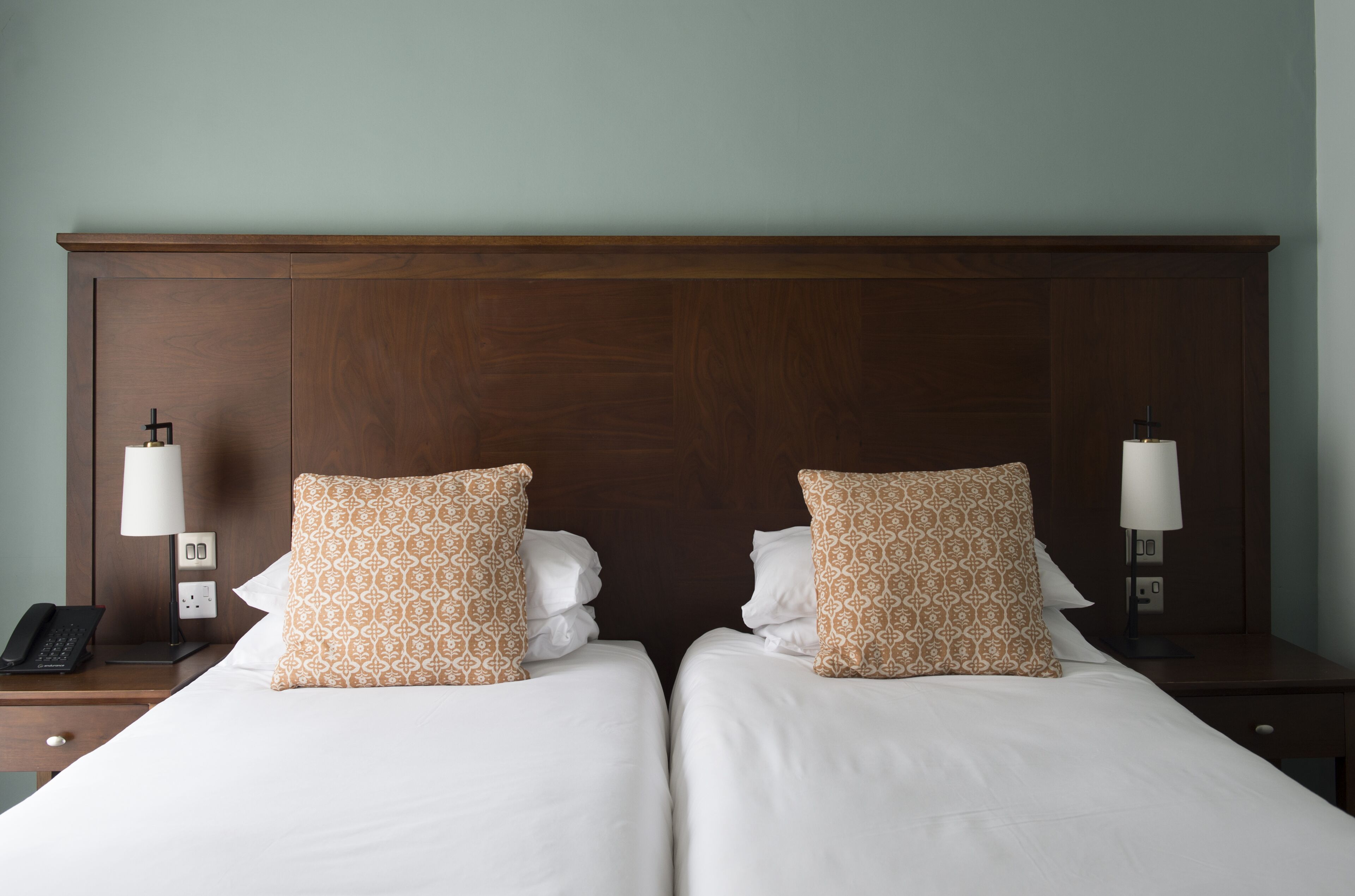A double bed with patterned pillows, a wooden headboard, bedside lamps, and a phone on the nightstand.