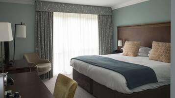 Een hotelkamer met een groot bed, een bureau met lamp, een stoel en uitzicht op de omgeving door het raam.