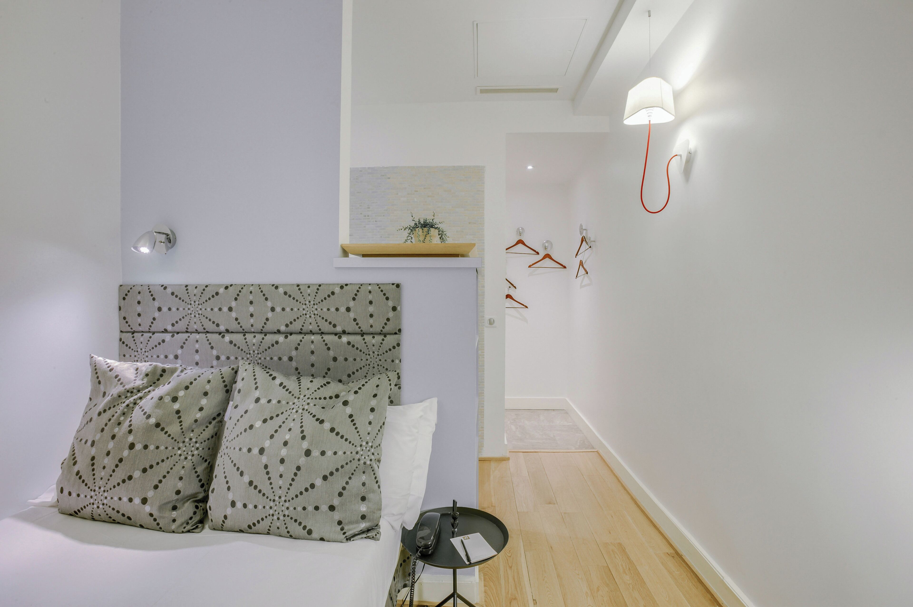 A bedroom with a bed, pillows, a bedside table with a phone, a lamp, and a wall-mounted light fixture.