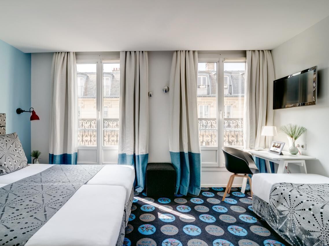 A hotel room with two beds, a desk, a TV, and a balcony view.