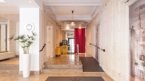 Un vestíbulo de hotel con suelo de mármol, un mostrador de recepción, una cortina roja y un candelabro.