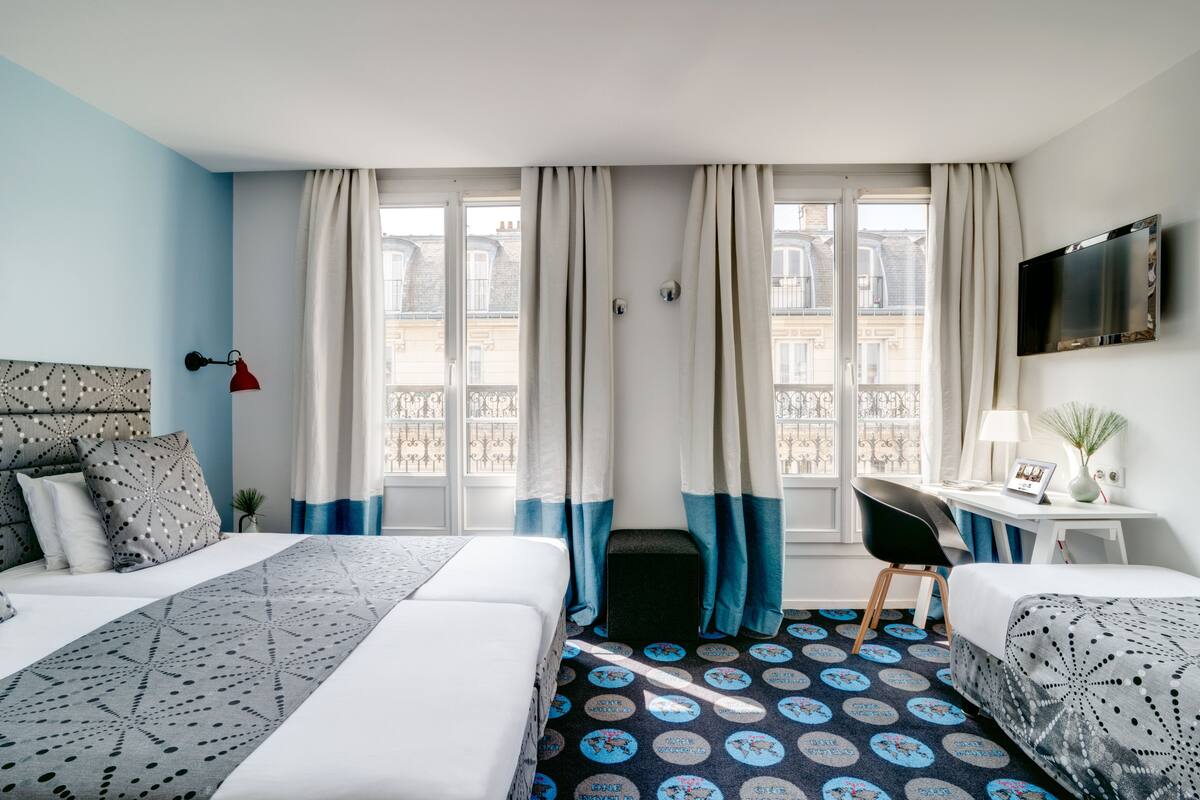 Une chambre d’hôtel avec un lit, un bureau, une chaise et un téléviseur fixé au mur.
