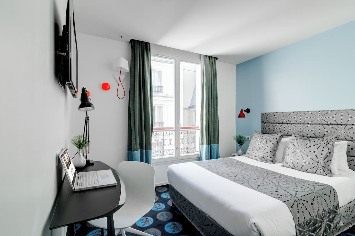 Une chambre d’hôtel avec un lit, un bureau, une chaise et une fenêtre avec des rideaux.