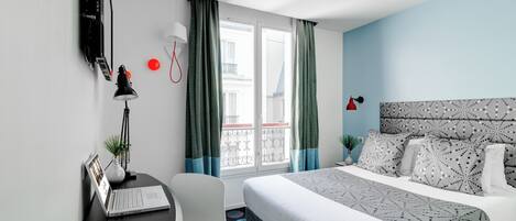 Une chambre d’hôtel avec un lit, un bureau, une chaise et une fenêtre avec des rideaux.