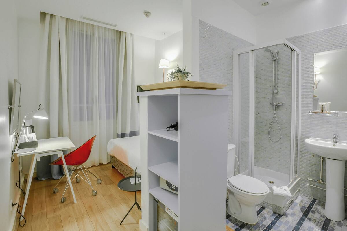 Une salle de bain moderne équipée d’une douche, de toilettes et d’un lavabo. On y trouve également un bureau avec une chaise et une lampe.