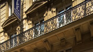 Fachada de hotel con elaboradas barandillas de hierro forjado, amplias ventanas y un letrero que dice "HOTEL ASTORIA OPERA".