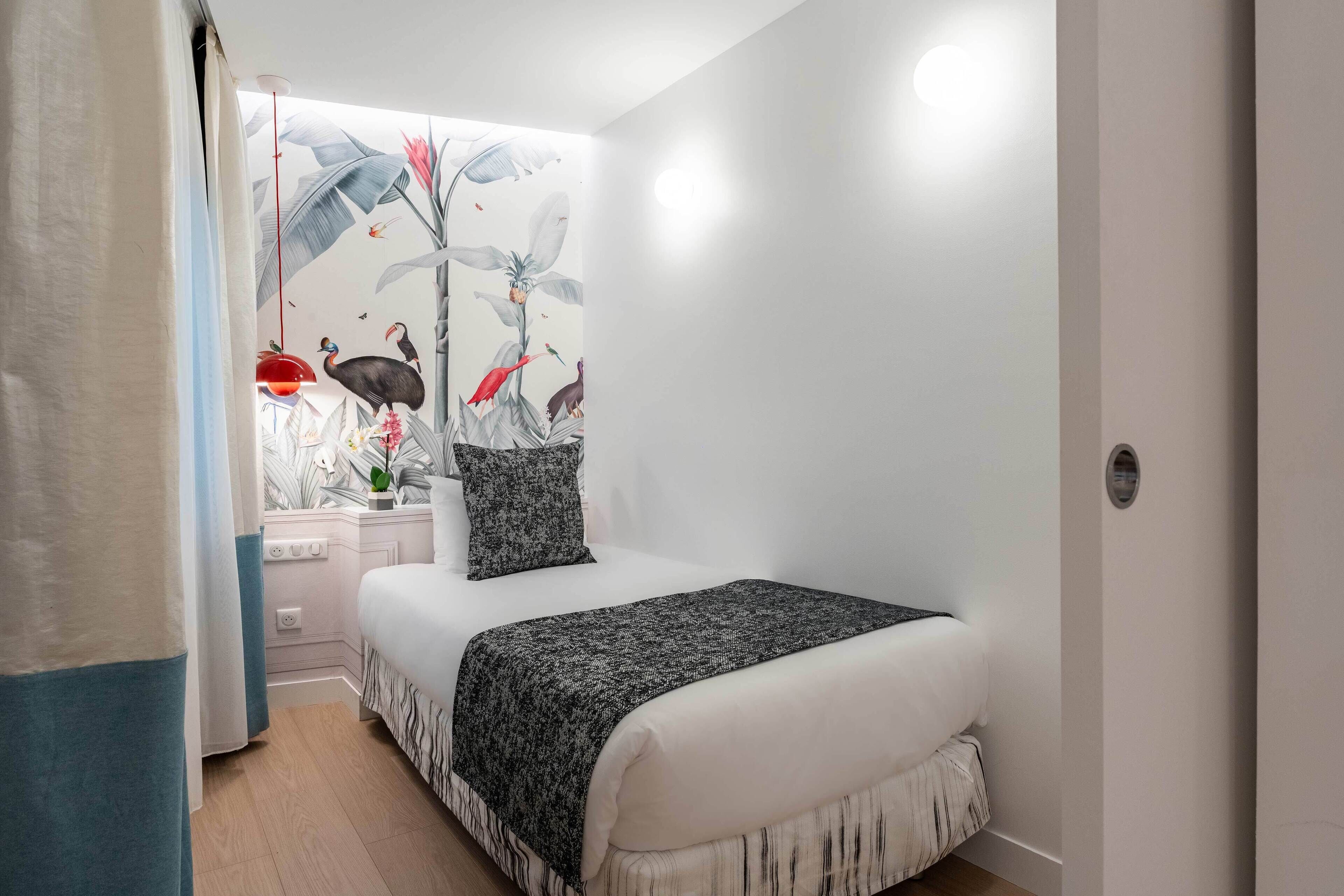 A bedroom with a bed, a nightstand, a lamp, and a wall mural.