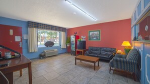 A living room with a sofa, a coffee table, a TV, and a lamp. - Mayfair Inn (Williamston)