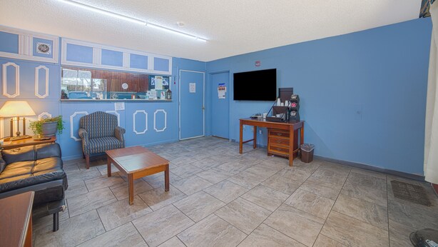 A room with a blue wall, a wooden table, a leather sofa, a chair, a television, and a desk with a computer. - Mayfair Inn (Williamston)
