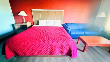 Una habitación de hotel con una cama grande, un sofá azul, una mesita de noche de madera y una pequeña mesa.