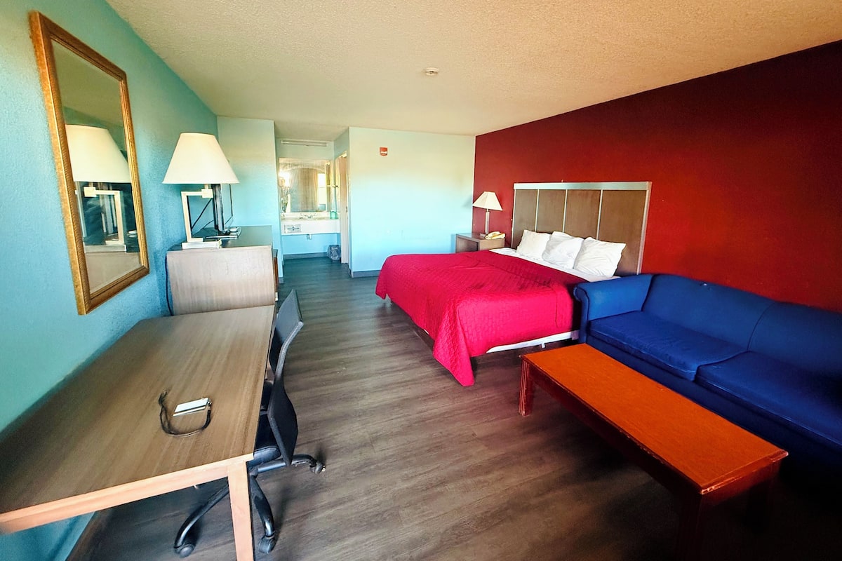 A hotel room with a bed, a blue sofa, a desk with a lamp, and a mirror.