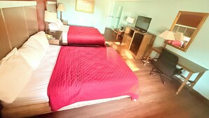 A hotel room with two beds, a desk, a chair, a TV, and a mirror. - Mayfair Inn (Williamston)