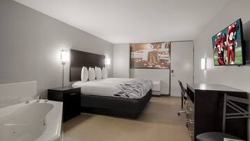 A modern hotel room with a large bed, a desk, a chair, a flat-screen TV, a large window, and a bathroom with a bathtub.