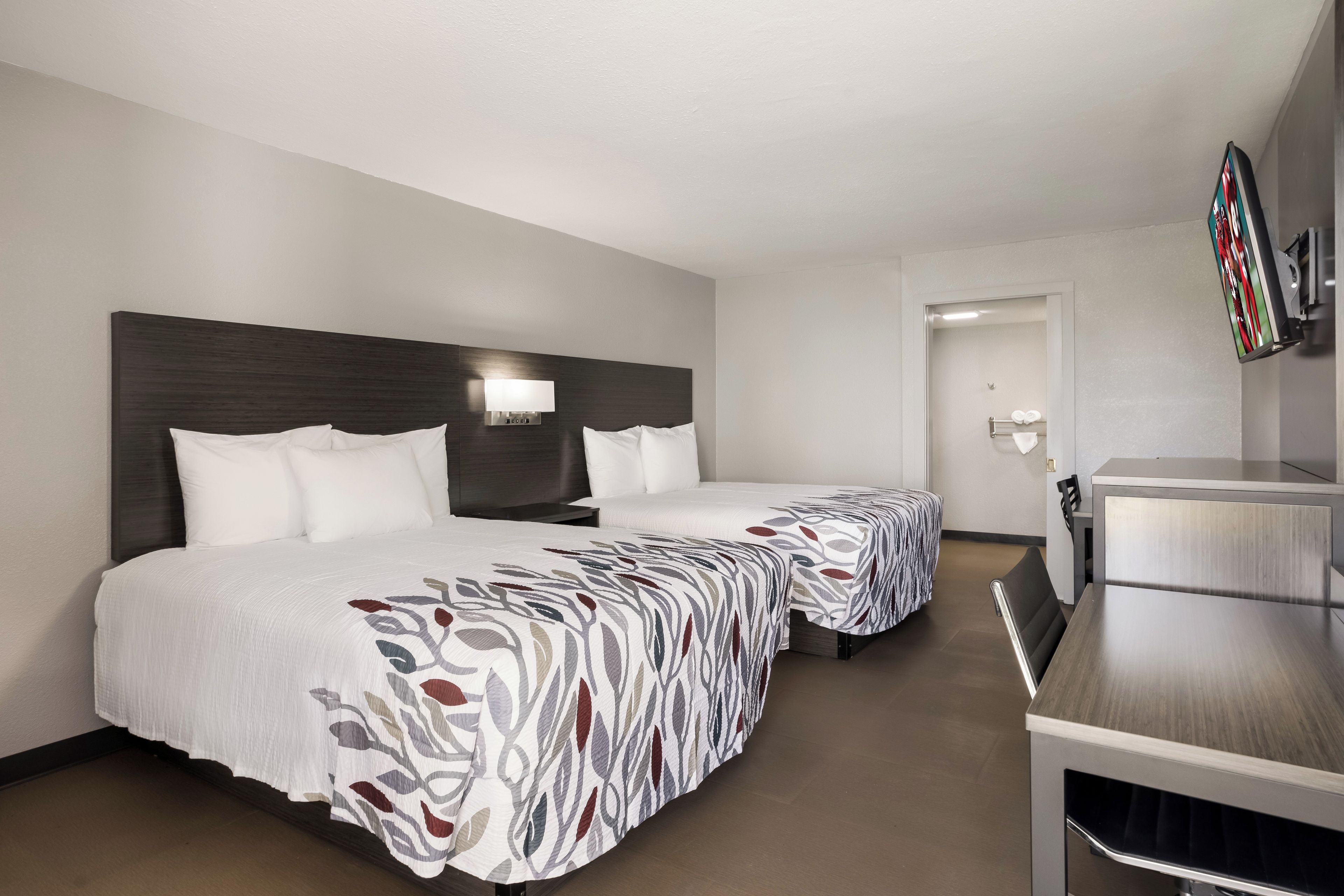 Habitación de hotel con dos camas, un escritorio y una televisión.