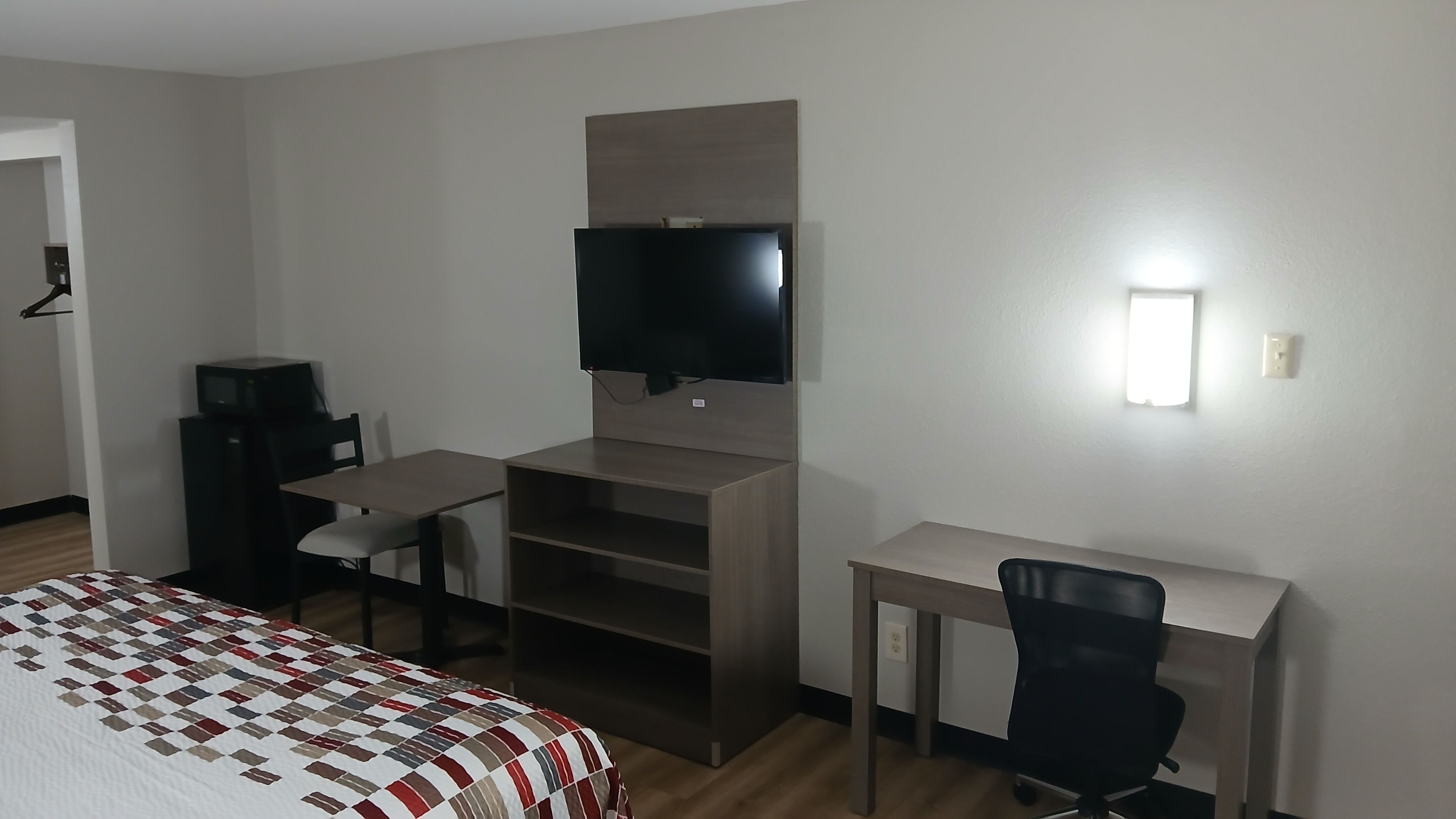 A hotel room with a bed, a desk, a chair, a television, and a shelf.