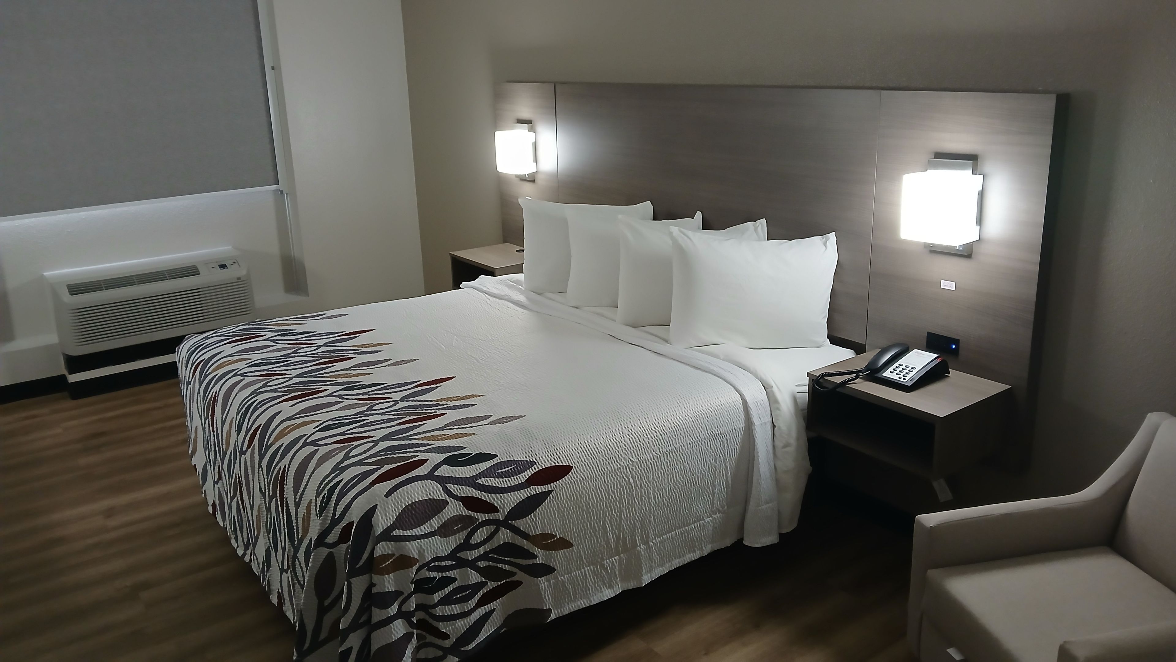 Quarto de hotel com uma cama grande, roupa de cama branca, telefone ao lado da cama e mesa de cabeceira.